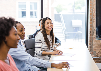 woman working at desk with colleagues in a meeting.